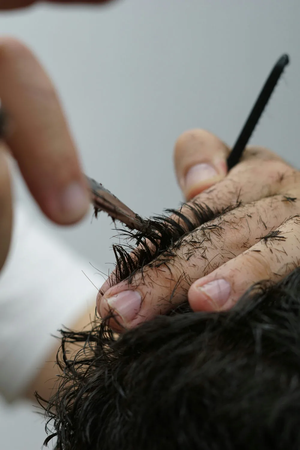 Mains coupant des cheveux noirs aux ciseaux, gros plan
